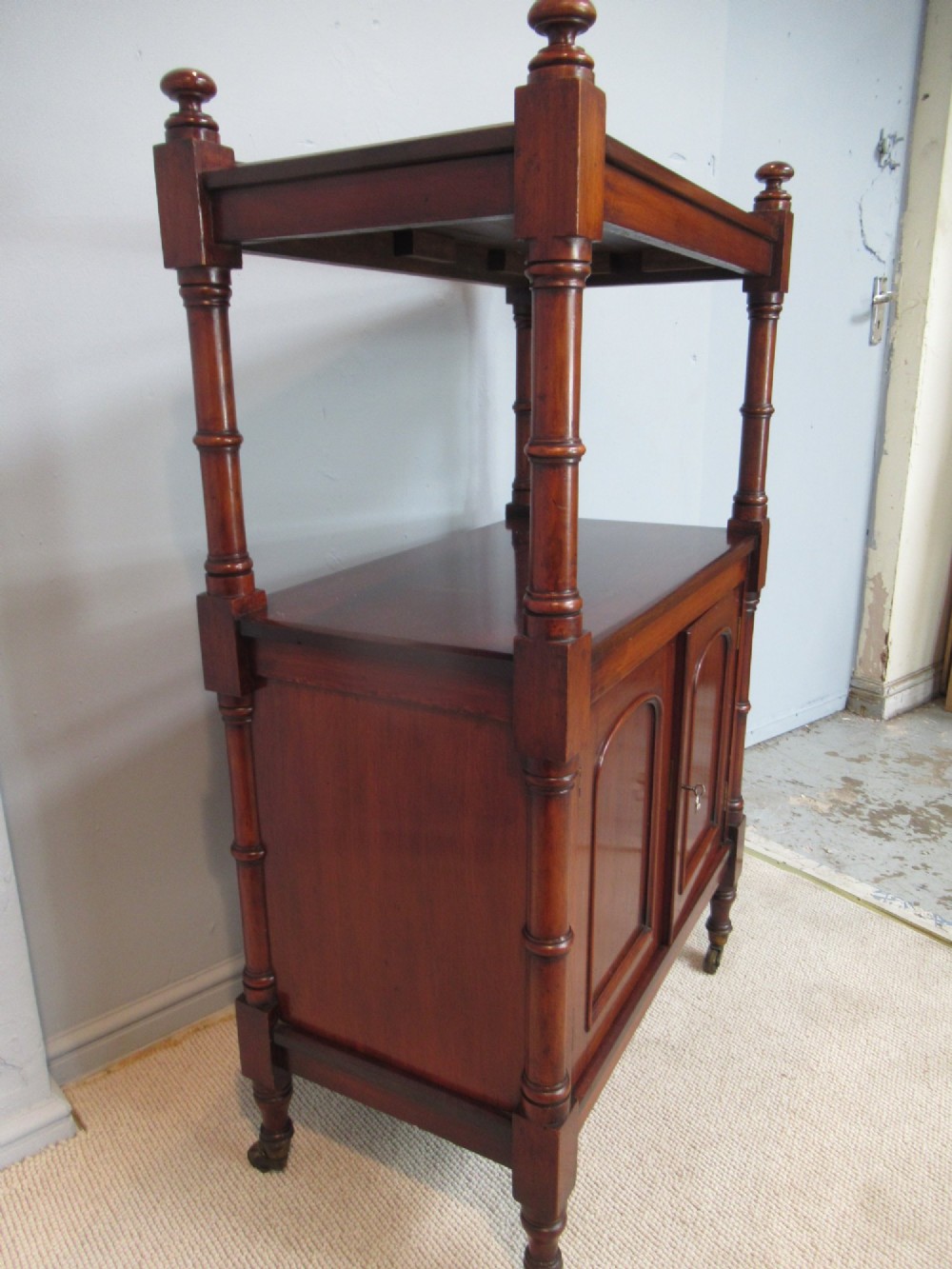 A Victorian mahogany chiffonier cabinet featuring a raised top tier supported by turned pillars above a two-door lower cupboard on brass castors. View IV