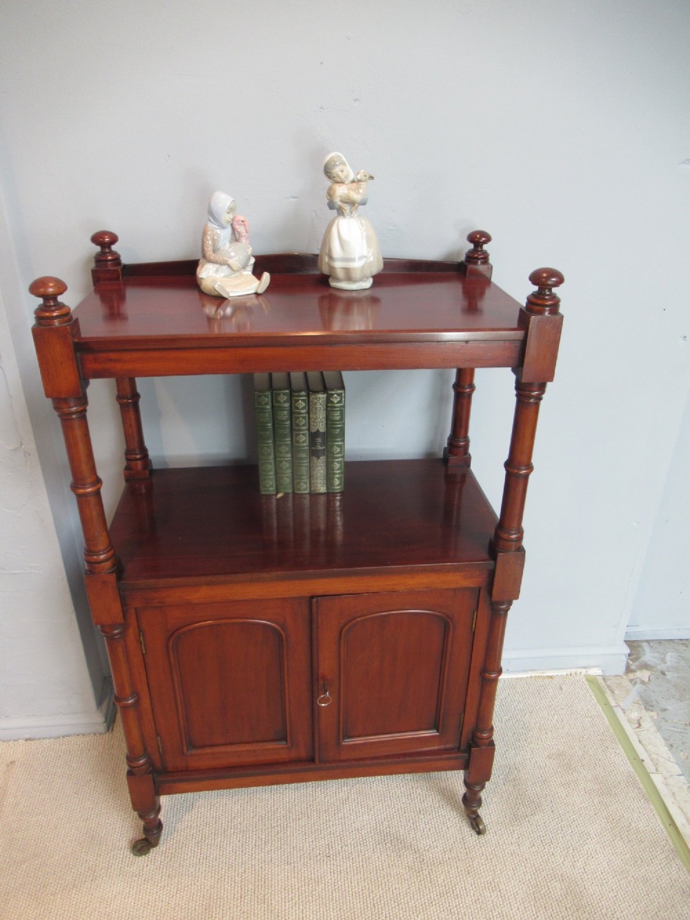 A Victorian mahogany chiffonier cabinet featuring a raised top tier supported by turned pillars above a two-door lower cupboard on brass castors. View VI