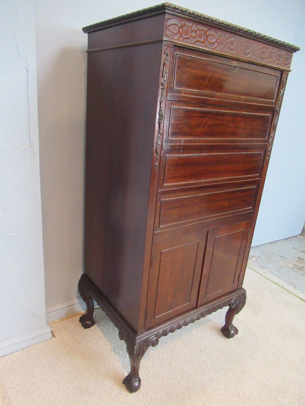 A tall, narrow dark mahogany music cabinet featuring fall-front drawer compartments, carved geometric fretwork, and cabriole legs ending in ball-and-claw feet. View III