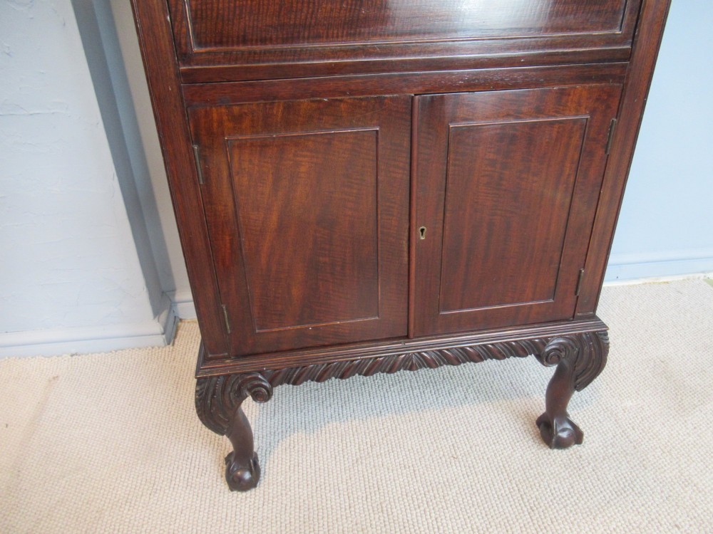A tall, narrow dark mahogany music cabinet featuring fall-front drawer compartments, carved geometric fretwork, and cabriole legs ending in ball-and-claw feet. View IV