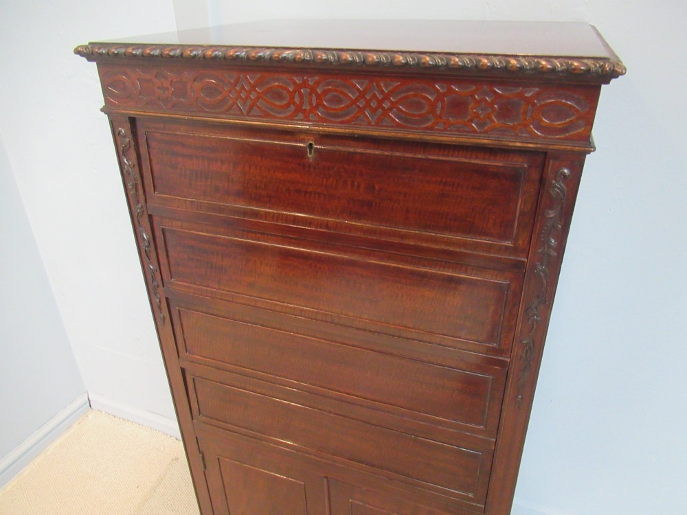 A tall, narrow dark mahogany music cabinet featuring fall-front drawer compartments, carved geometric fretwork, and cabriole legs ending in ball-and-claw feet. View V