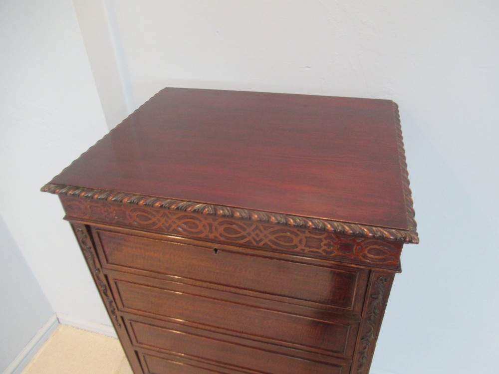 A tall, narrow dark mahogany music cabinet featuring fall-front drawer compartments, carved geometric fretwork, and cabriole legs ending in ball-and-claw feet. View VI