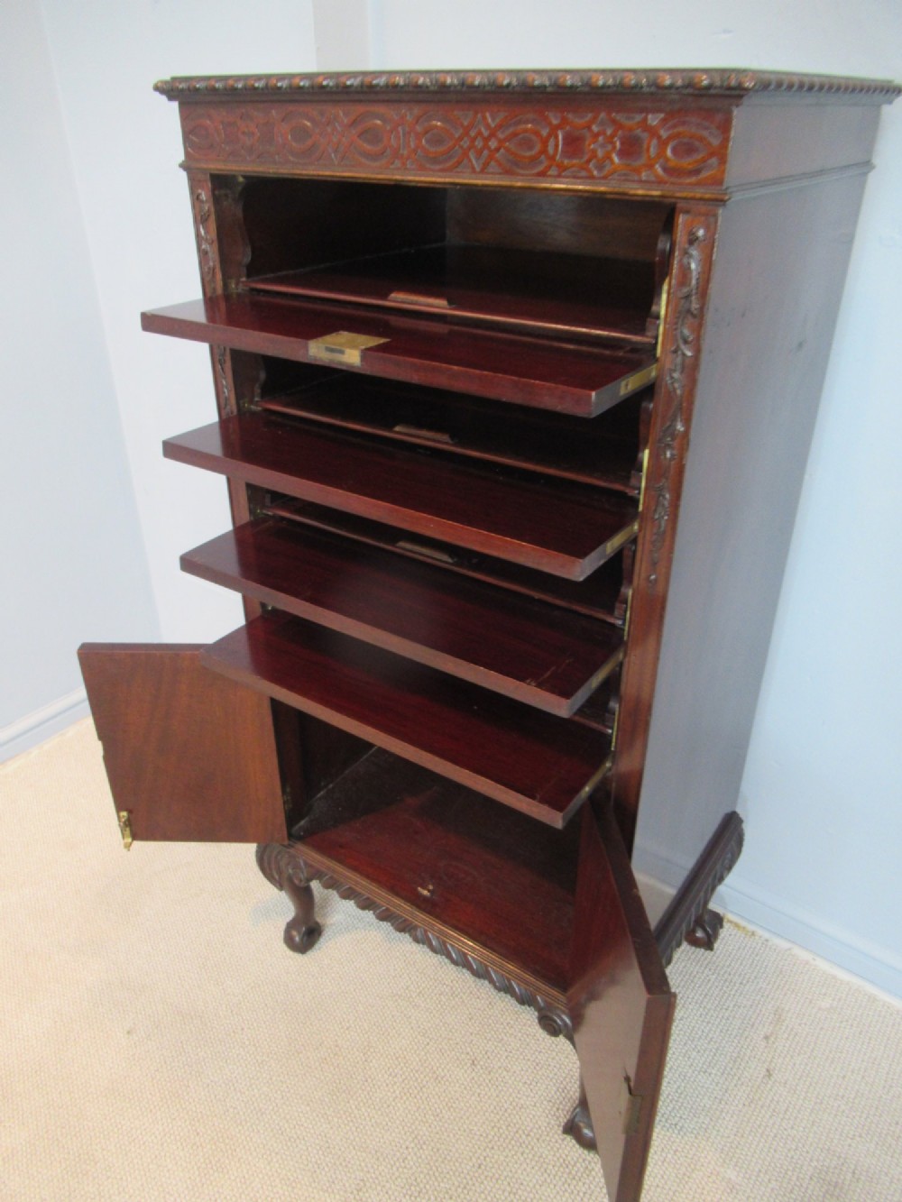 A tall, narrow dark mahogany music cabinet featuring fall-front drawer compartments, carved geometric fretwork, and cabriole legs ending in ball-and-claw feet. View VII