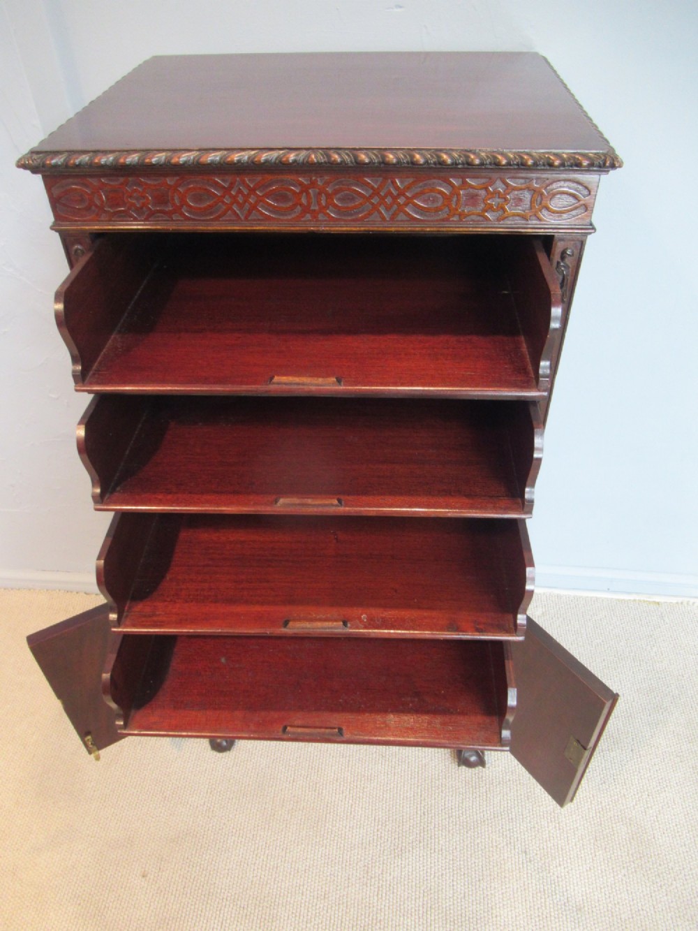 A tall, narrow dark mahogany music cabinet featuring fall-front drawer compartments, carved geometric fretwork, and cabriole legs ending in ball-and-claw feet. View IX