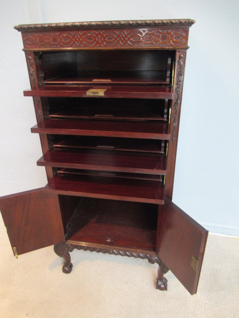 A tall, narrow dark mahogany music cabinet featuring fall-front drawer compartments, carved geometric fretwork, and cabriole legs ending in ball-and-claw feet. View X