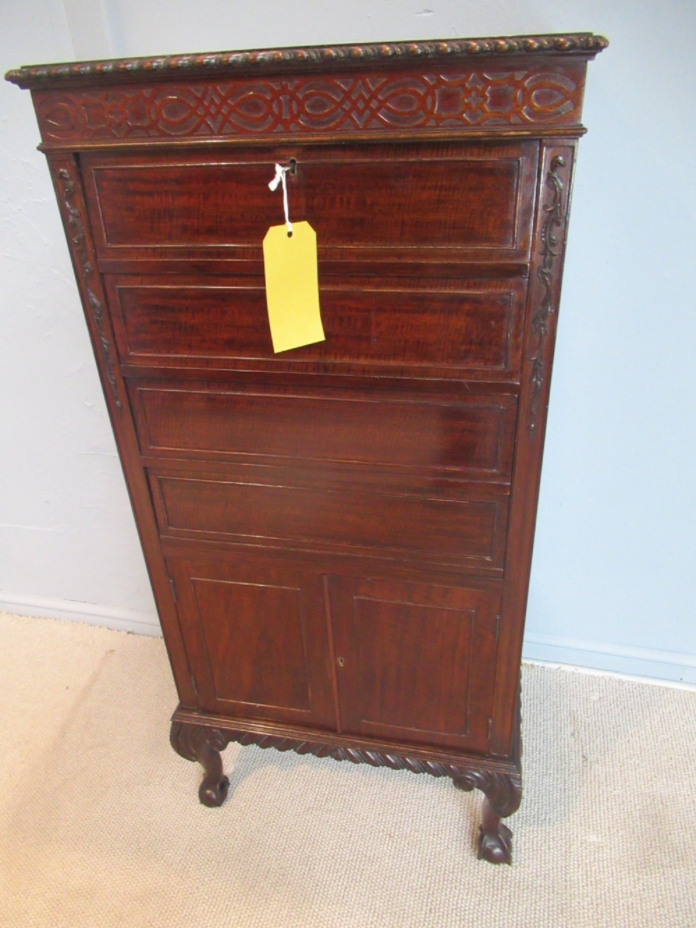 A tall, narrow dark mahogany music cabinet featuring fall-front drawer compartments, carved geometric fretwork, and cabriole legs ending in ball-and-claw feet. View XI