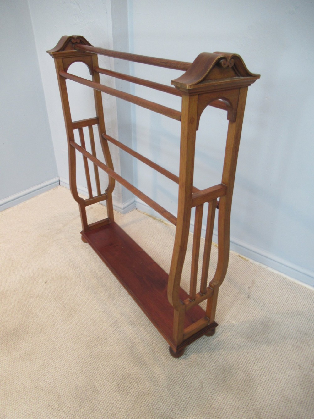 A freestanding Victorian walnut towel rail featuring carved end supports, curved pediment top caps, multiple horizontal wooden rungs, and a flat lower shelf.