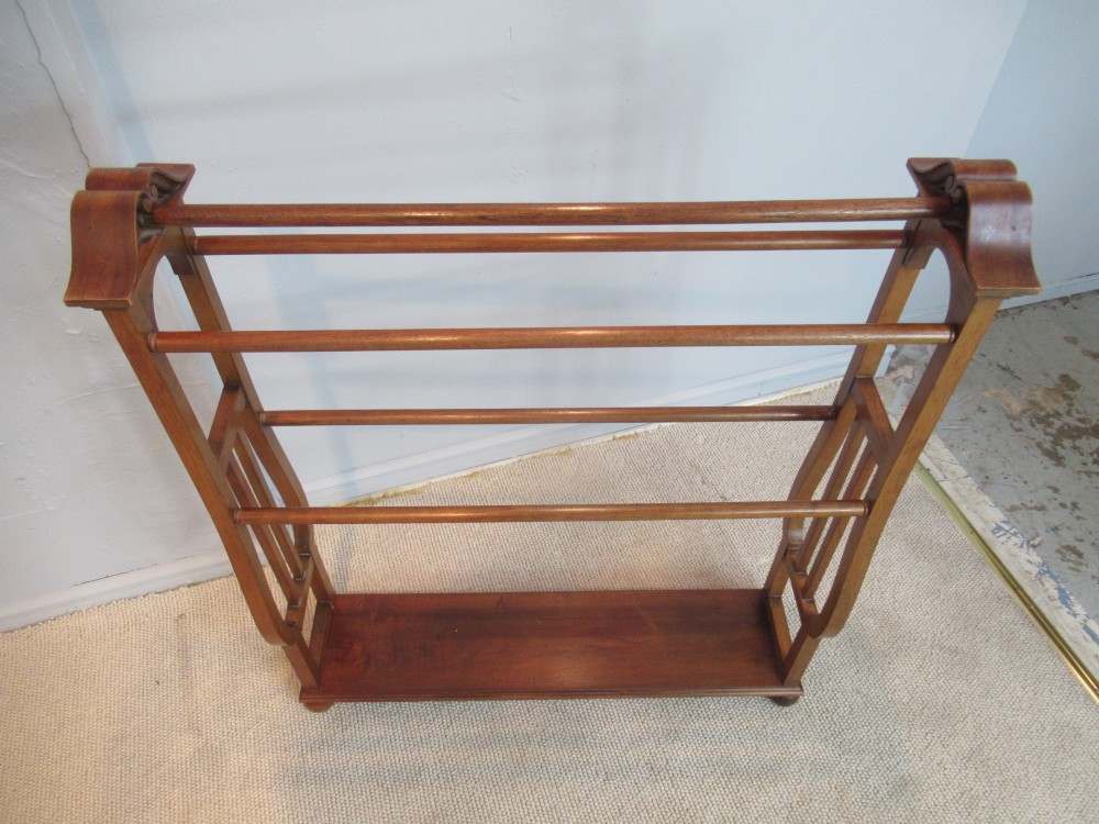 A freestanding Victorian walnut towel rail featuring carved end supports, curved pediment top caps, multiple horizontal wooden rungs, and a flat lower shelf. View V