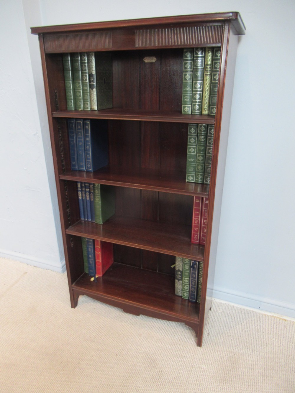 An antique dark mahogany open bookcase featuring four adjustable shelves, fluted frieze detailing at the top, and bracket feet.