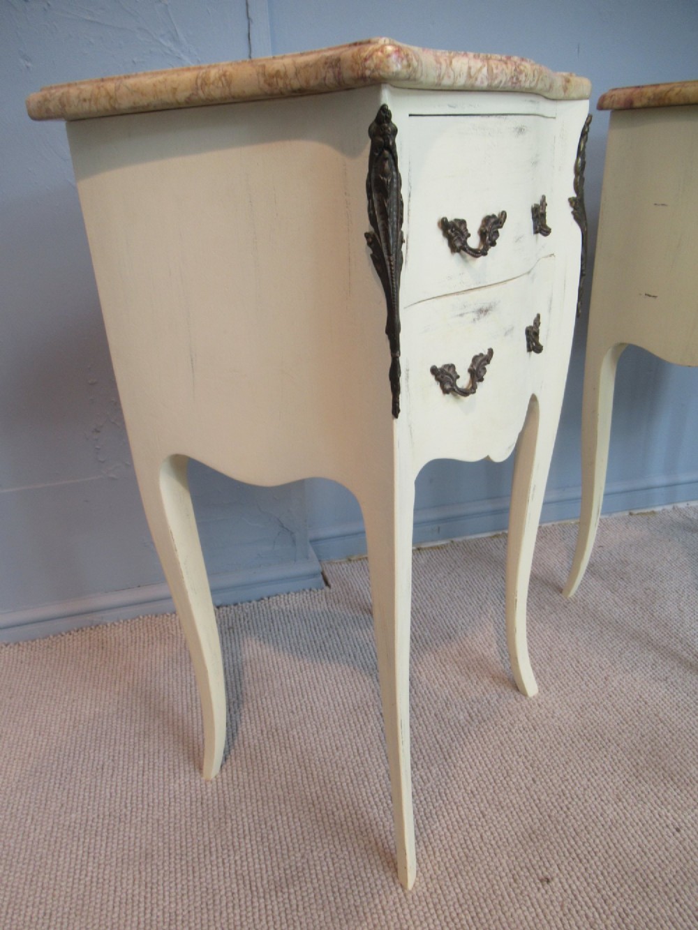 A pair of cream painted French style bedside cabinets featuring variegated marble tops, two drawers with brass handles, and slender cabriole legs. View V