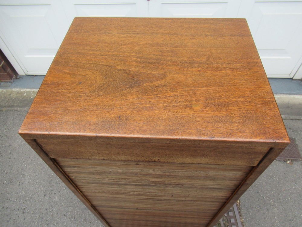 A tall, vertical mahogany filing cabinet with a closed flexible slat tambour front door and a dark handle at the bottom base. View V