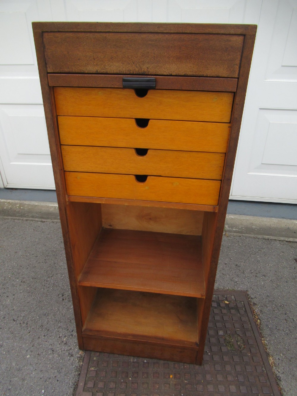 A tall, vertical mahogany filing cabinet with a closed flexible slat tambour front door and a dark handle at the bottom base. View VI