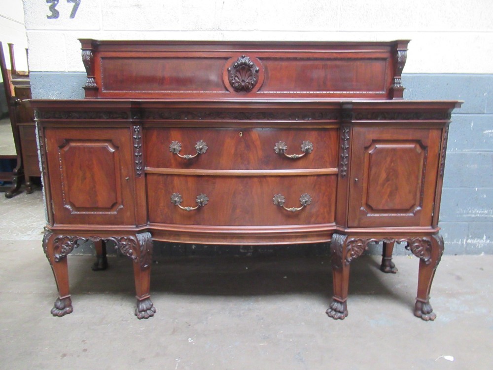 An Edwardian carved mahogany sideboard featuring a raised backboard with a carved shell motif, central bow-front drawers, side cupboard doors, and cabriole legs with ball and claw feet.