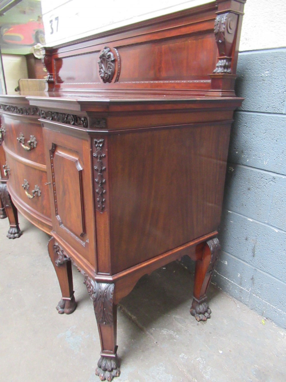 An Edwardian carved mahogany sideboard featuring a raised backboard with a carved shell motif, central bow-front drawers, side cupboard doors, and cabriole legs with ball and claw feet. View IV