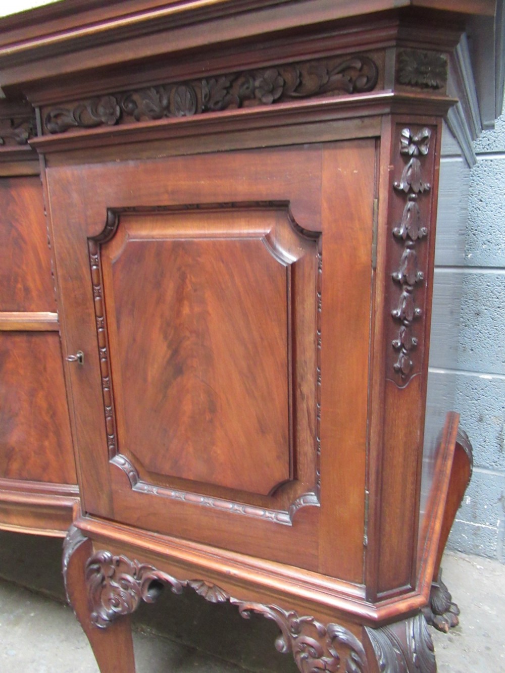 An Edwardian carved mahogany sideboard featuring a raised backboard with a carved shell motif, central bow-front drawers, side cupboard doors, and cabriole legs with ball and claw feet. View VII
