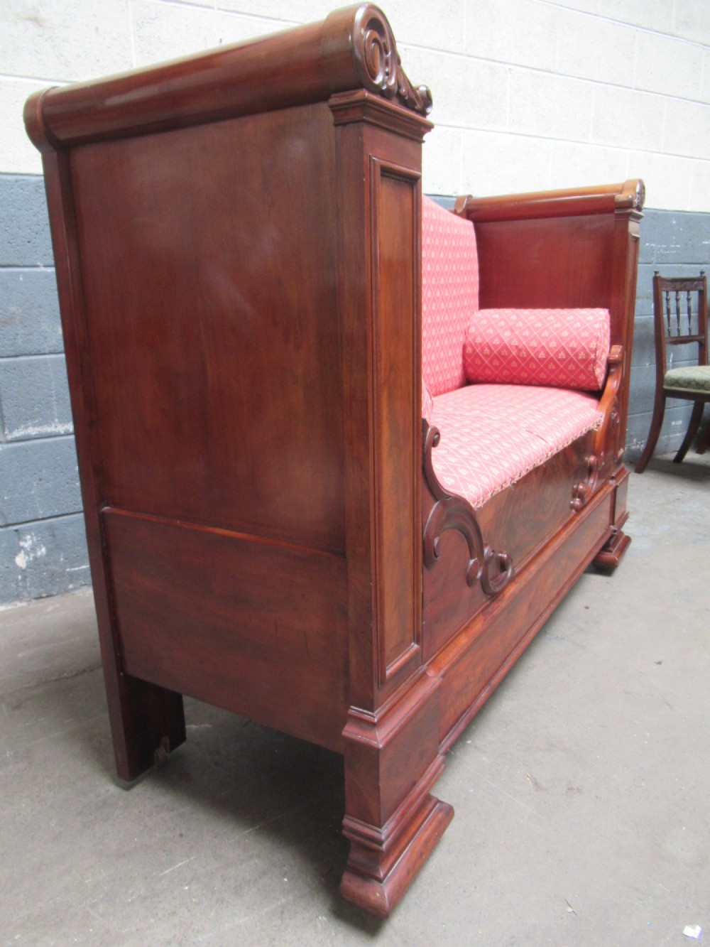 A 19th-century mahogany upholstered bench featuring scrolled armrests, flame mahogany veneered panelling, and red patterned fabric seating with bolster cushions. View III
