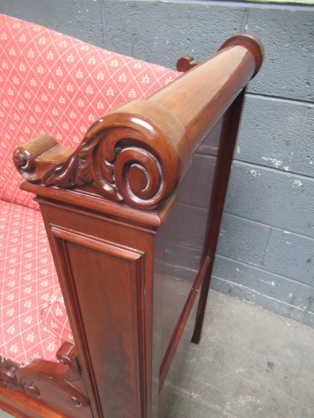A 19th-century mahogany upholstered bench featuring scrolled armrests, flame mahogany veneered panelling, and red patterned fabric seating with bolster cushions. View VI