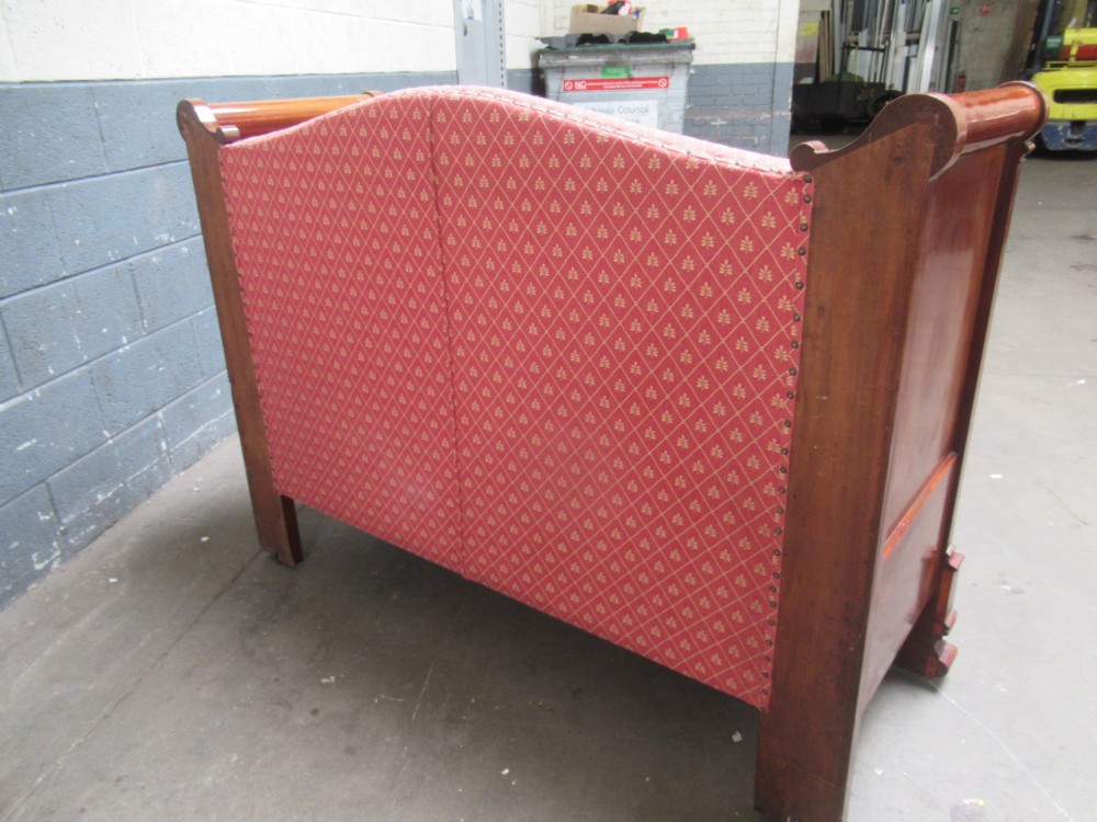 A 19th-century mahogany upholstered bench featuring scrolled armrests, flame mahogany veneered panelling, and red patterned fabric seating with bolster cushions. View X