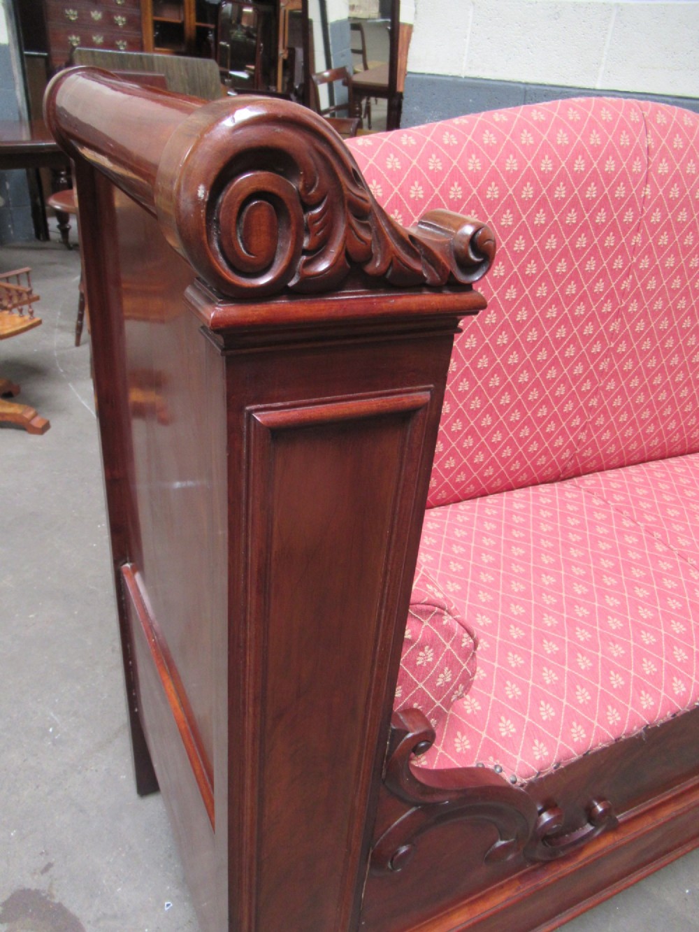 A 19th-century mahogany upholstered bench featuring scrolled armrests, flame mahogany veneered panelling, and red patterned fabric seating with bolster cushions. View XI