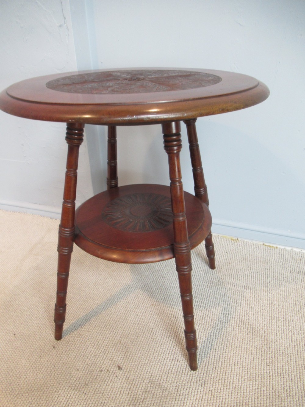 A round Victorian mahogany side table featuring a carved top, turned spindle legs, and a lower carved shelf.