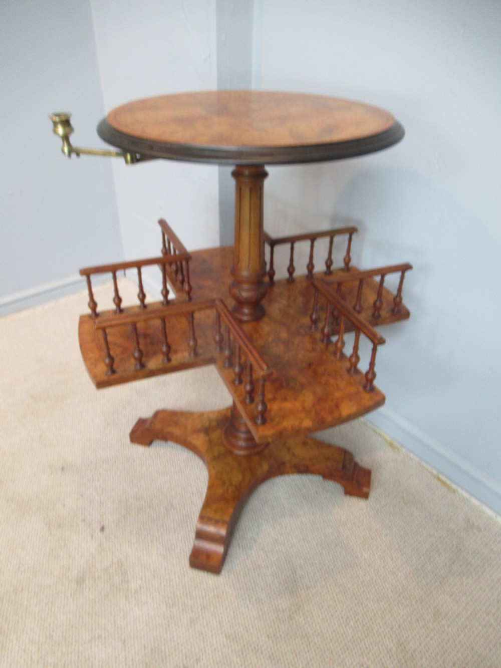 A 19th-century burr walnut revolving bookstand featuring a circular top with an attached brass candle arm, set above a spindled four-compartment revolving shelf and a quadripartite pedestal base.