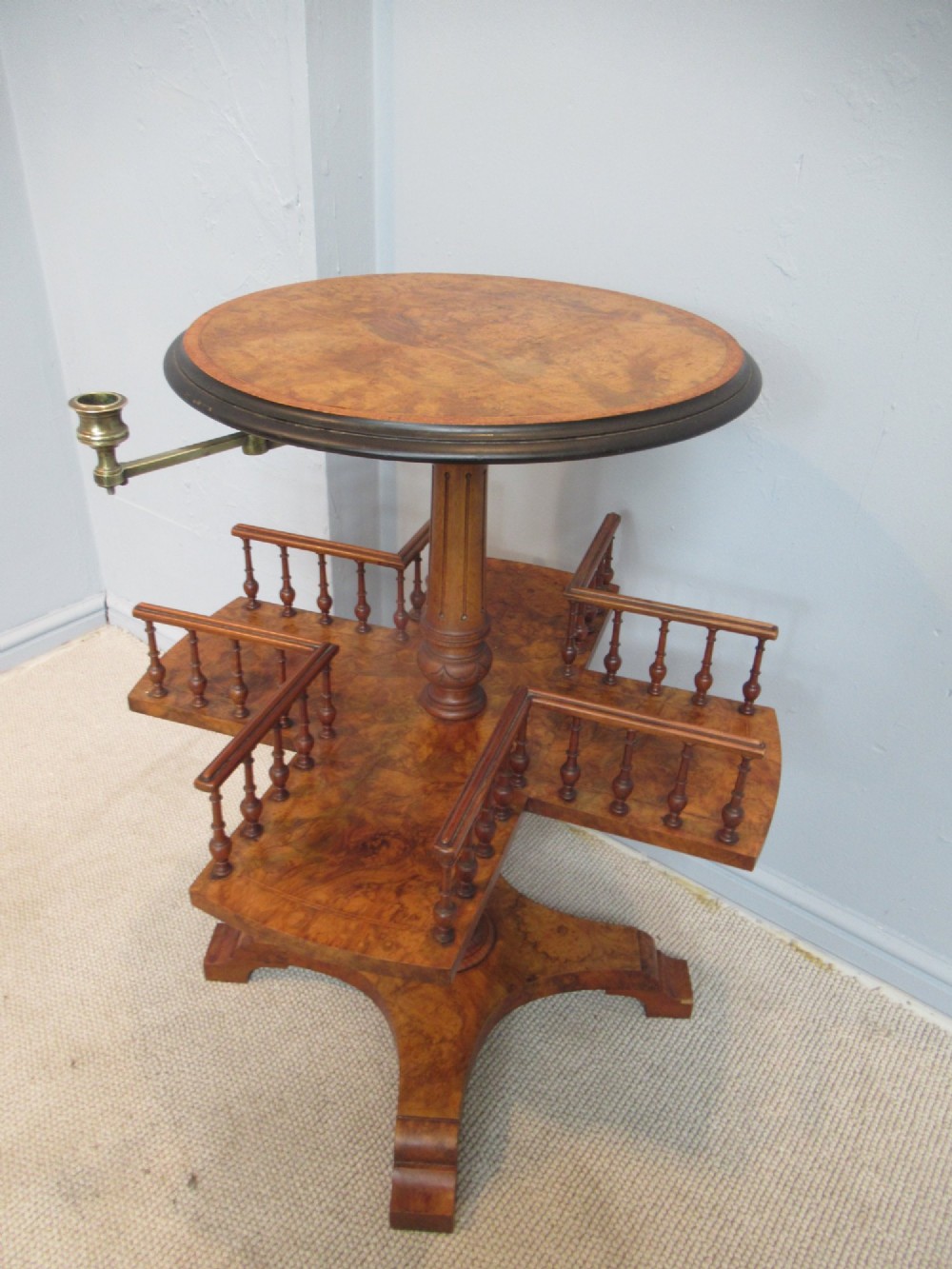 A 19th-century burr walnut revolving bookstand featuring a circular top with an attached brass candle arm, set above a spindled four-compartment revolving shelf and a quadripartite pedestal base. View II