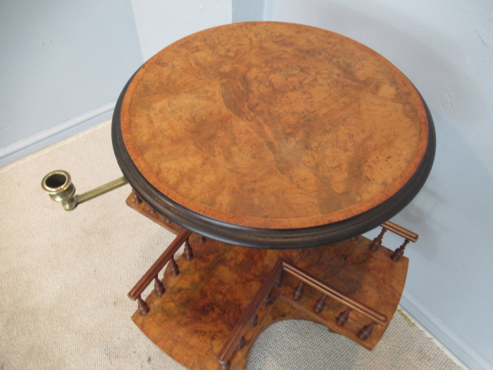 A 19th-century burr walnut revolving bookstand featuring a circular top with an attached brass candle arm, set above a spindled four-compartment revolving shelf and a quadripartite pedestal base. View III