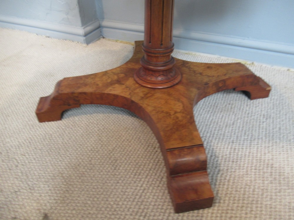 A 19th-century burr walnut revolving bookstand featuring a circular top with an attached brass candle arm, set above a spindled four-compartment revolving shelf and a quadripartite pedestal base. View IV