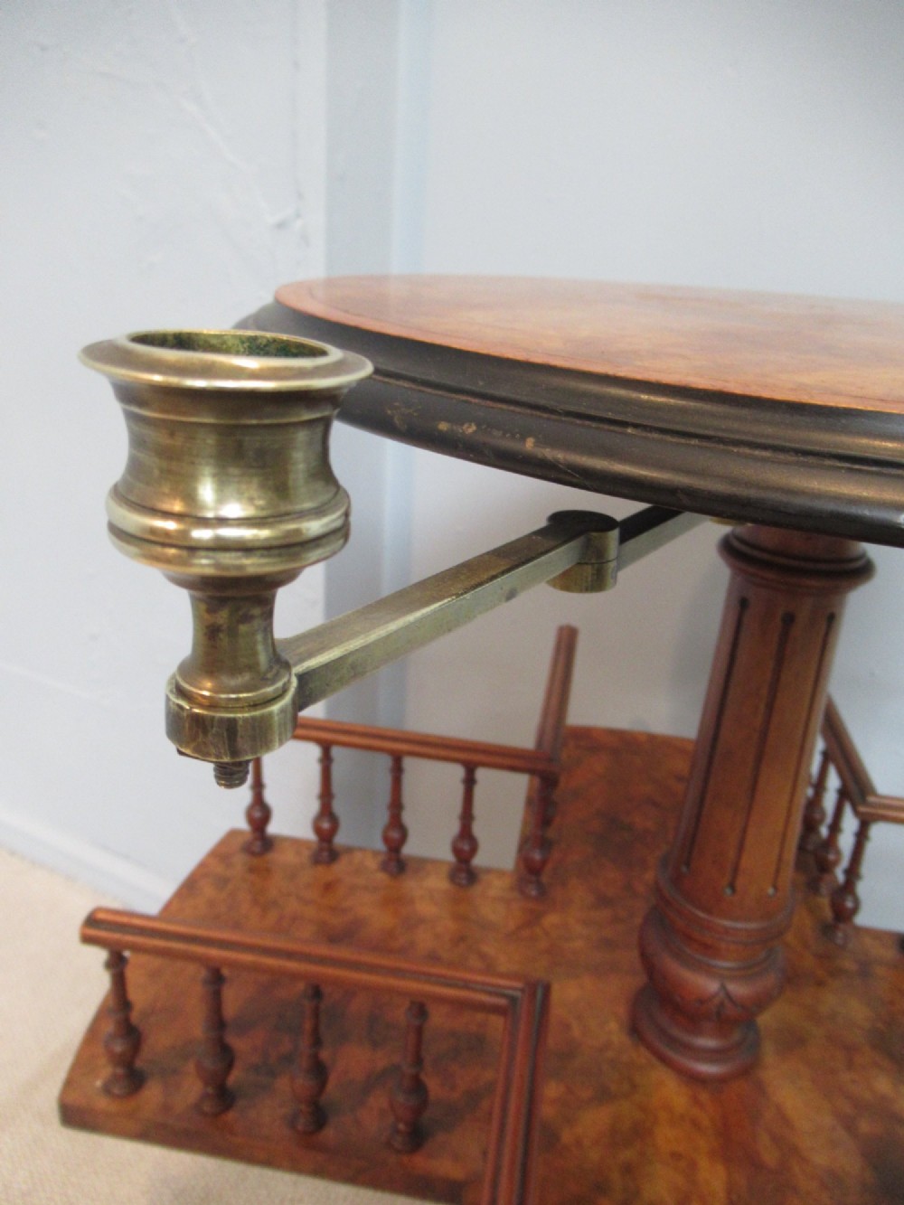 A 19th-century burr walnut revolving bookstand featuring a circular top with an attached brass candle arm, set above a spindled four-compartment revolving shelf and a quadripartite pedestal base. View V