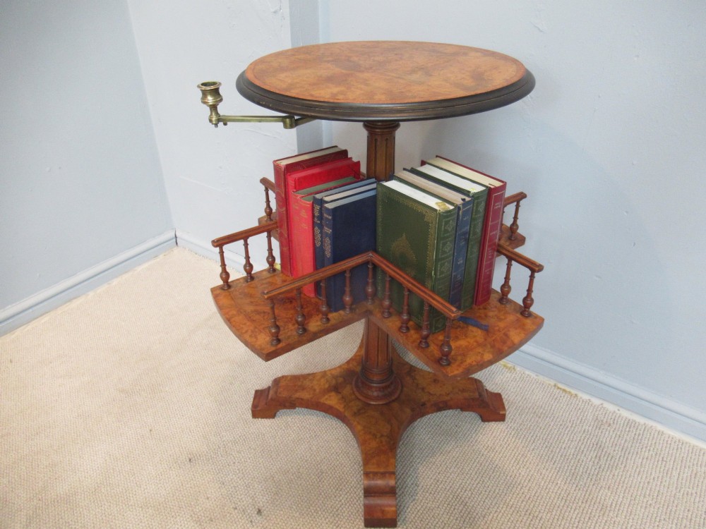 A 19th-century burr walnut revolving bookstand featuring a circular top with an attached brass candle arm, set above a spindled four-compartment revolving shelf and a quadripartite pedestal base. View VI