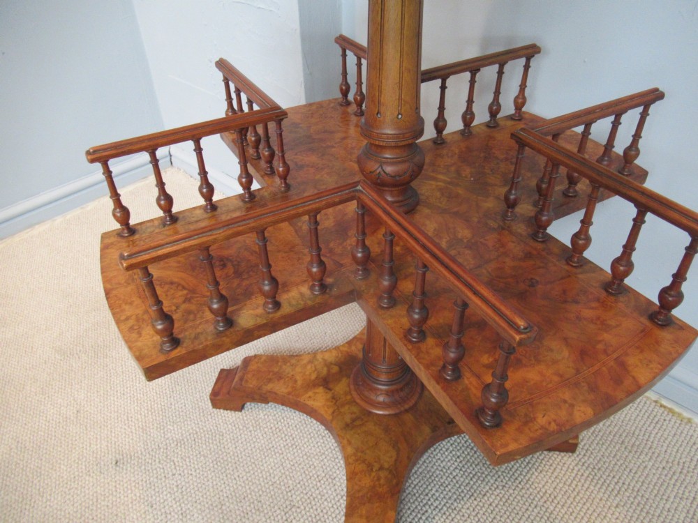A 19th-century burr walnut revolving bookstand featuring a circular top with an attached brass candle arm, set above a spindled four-compartment revolving shelf and a quadripartite pedestal base. View VII