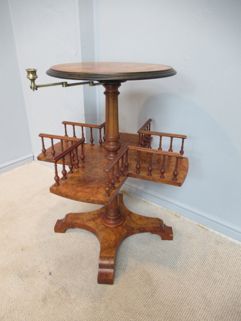 A 19th-century burr walnut revolving bookstand featuring a circular top with an attached brass candle arm, set above a spindled four-compartment revolving shelf and a quadripartite pedestal base. View VIII