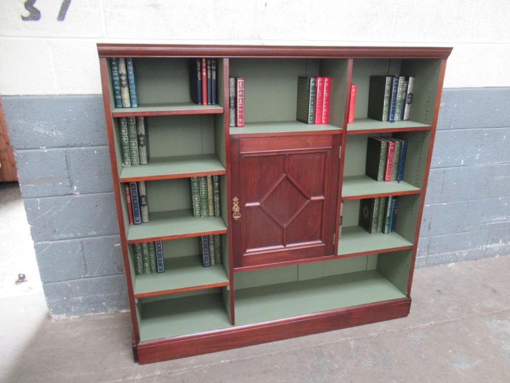An Edwardian mahogany open bookcase with asymmetrical sage green painted shelves and a central panelled cupboard door featuring diamond moulding.