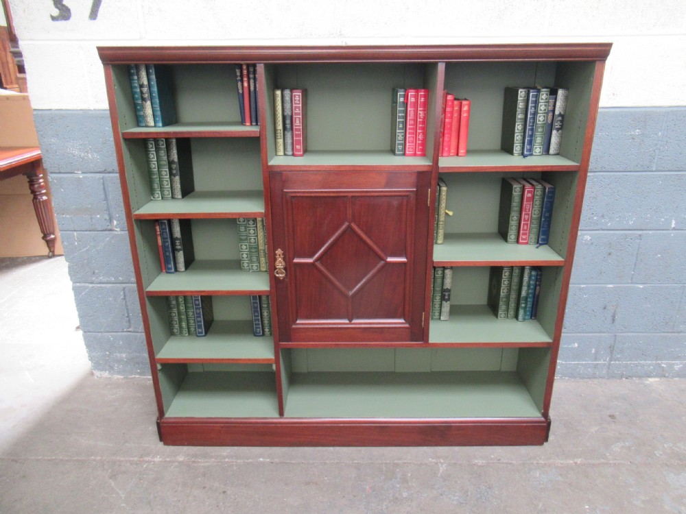 An Edwardian mahogany open bookcase with asymmetrical sage green painted shelves and a central panelled cupboard door featuring diamond moulding. View II