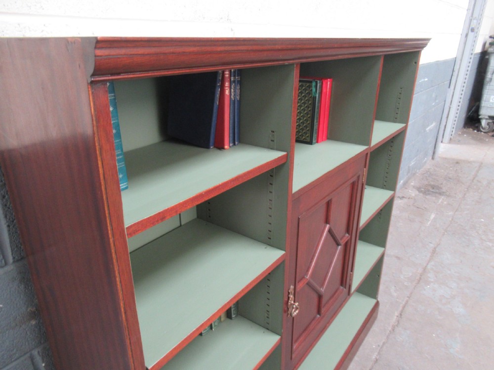 An Edwardian mahogany open bookcase with asymmetrical sage green painted shelves and a central panelled cupboard door featuring diamond moulding. View X