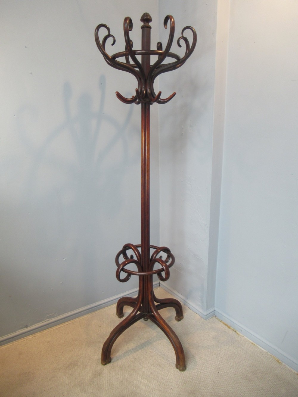 A dark brown bentwood hat and coat stand featuring multiple curved upper hooks, a central turned pole, a lower umbrella ring, and splayed legs. View II