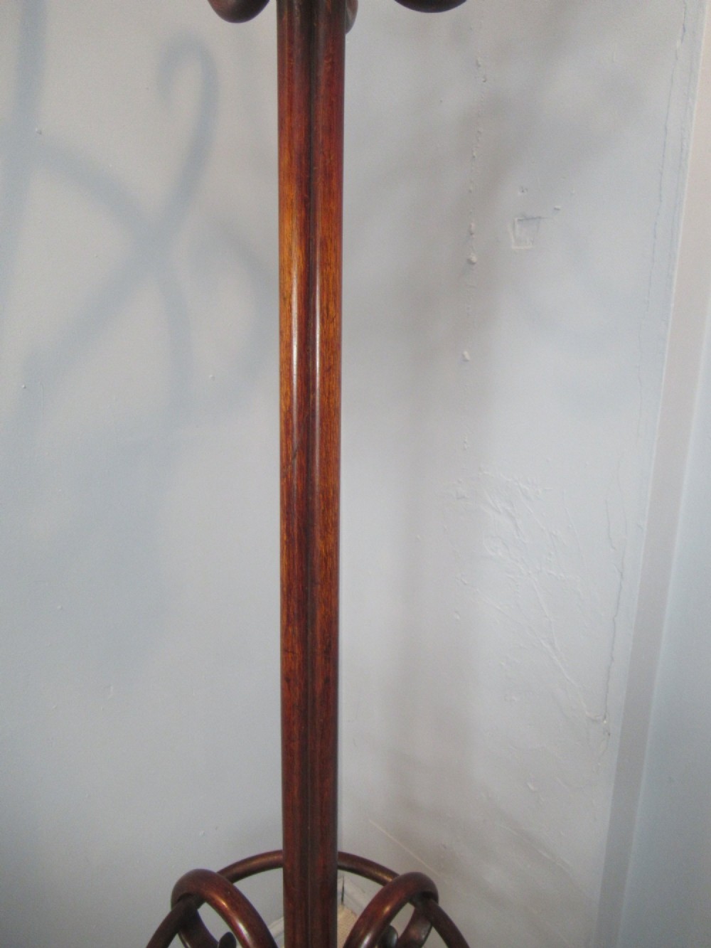 A dark brown bentwood hat and coat stand featuring multiple curved upper hooks, a central turned pole, a lower umbrella ring, and splayed legs. View VI