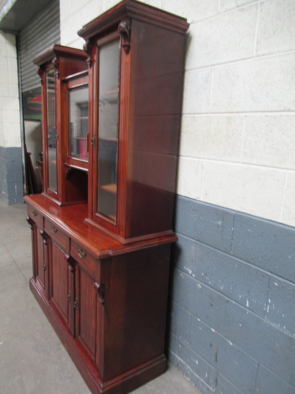 Late Victorian mahogany bookcase featuring glazed upper cabinet sections, carved corbels, fluted pilasters, drawers, and lower panelled doors. View IV