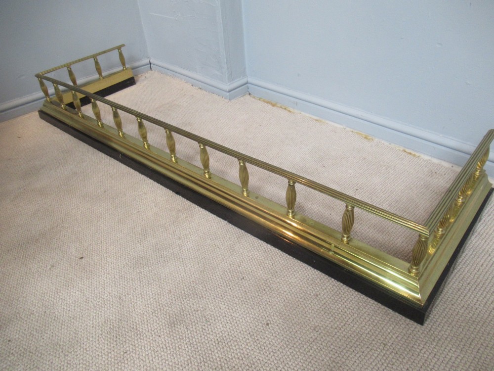 A late Victorian brass and iron fire fender featuring a polished brass top rail with fluted baluster uprights on a heavy black base.