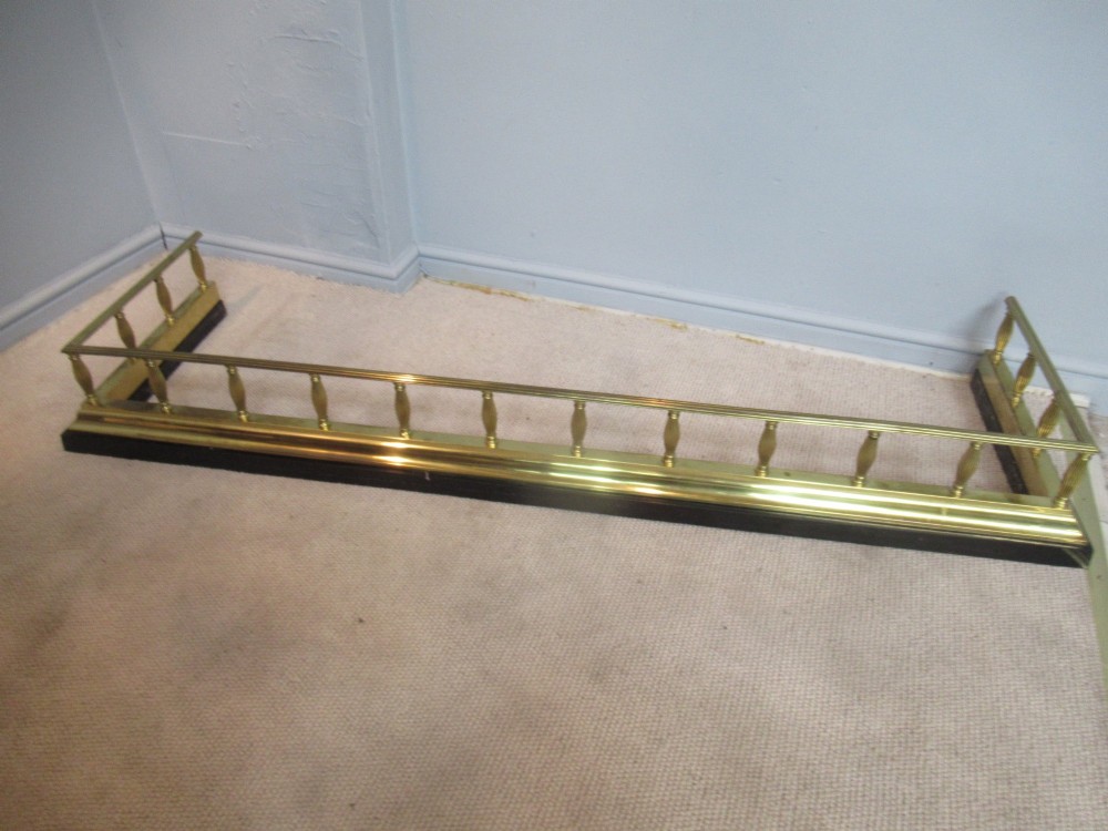 A late Victorian brass and iron fire fender featuring a polished brass top rail with fluted baluster uprights on a heavy black base. View II