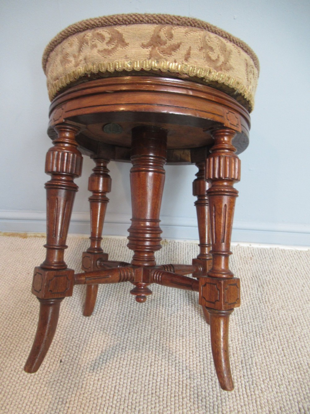 A Victorian walnut revolving piano stool featuring fluted carved legs, cross-stretchers, and a circular padded tapestry upholstered seat.