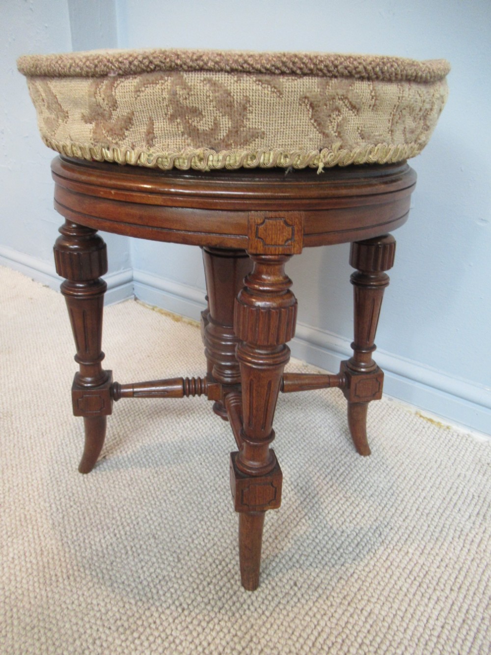 A Victorian walnut revolving piano stool featuring fluted carved legs, cross-stretchers, and a circular padded tapestry upholstered seat. View II