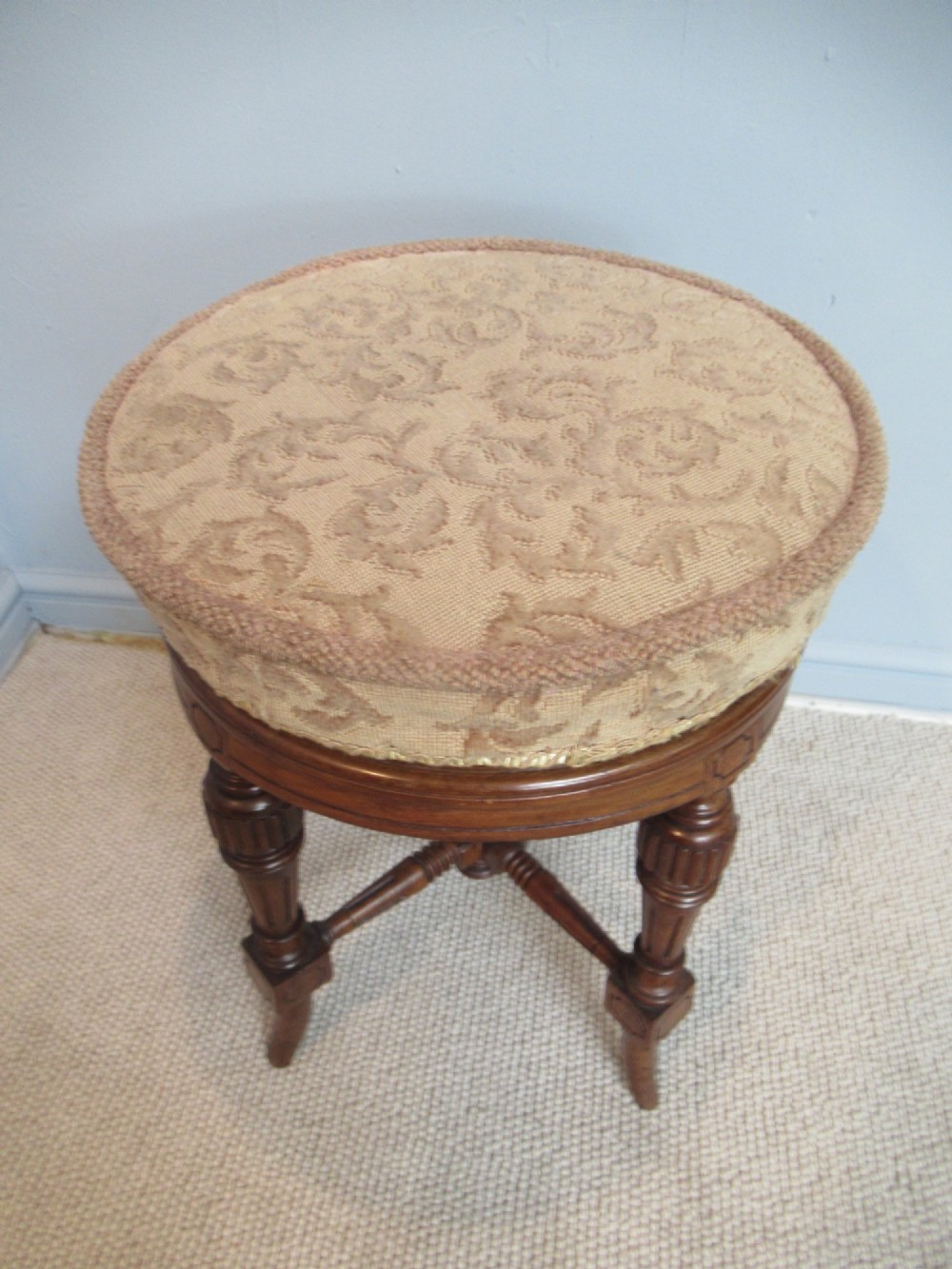 A Victorian walnut revolving piano stool featuring fluted carved legs, cross-stretchers, and a circular padded tapestry upholstered seat. View III