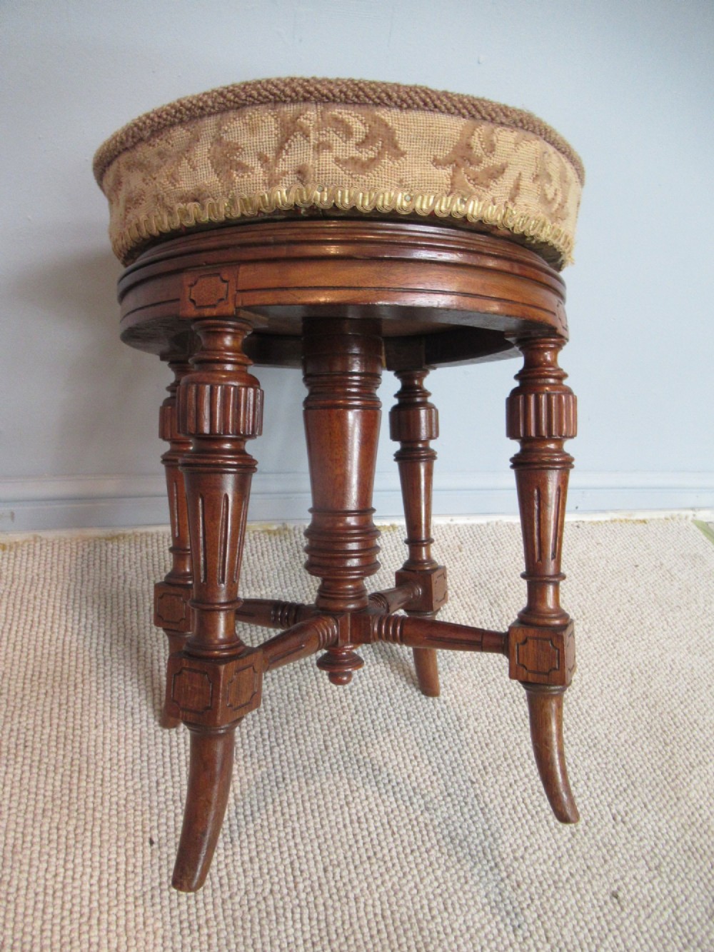A Victorian walnut revolving piano stool featuring fluted carved legs, cross-stretchers, and a circular padded tapestry upholstered seat. View IV