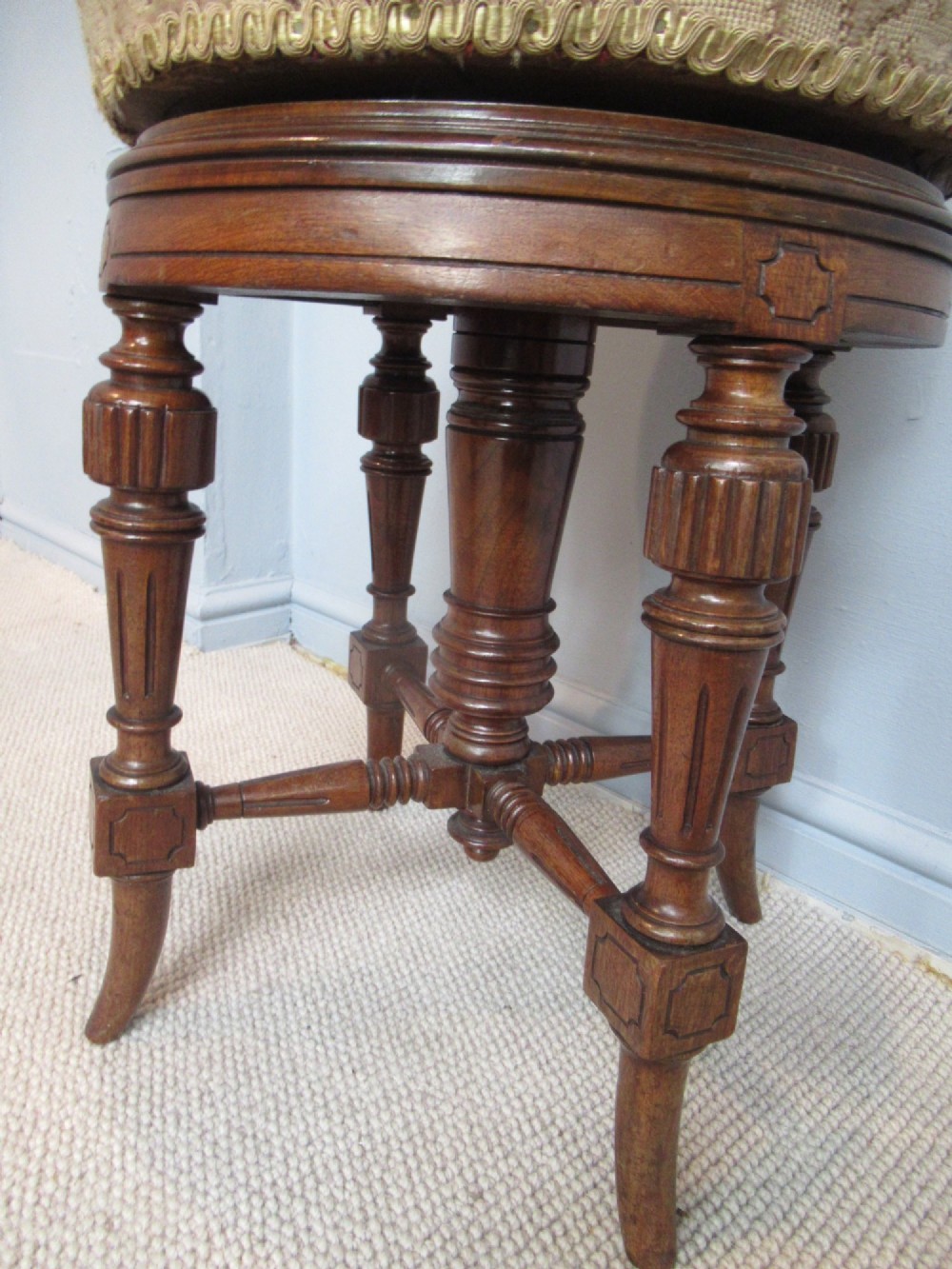 A Victorian walnut revolving piano stool featuring fluted carved legs, cross-stretchers, and a circular padded tapestry upholstered seat. View VII