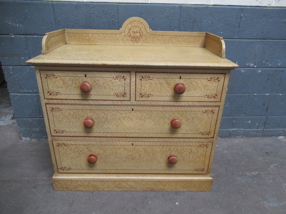 A Victorian painted pine chest of drawers with two short over two long drawers, decorated with scumbled graining, red stencilled borders, turned wooden knobs, and an upstand inscribed New Year Day 1894.