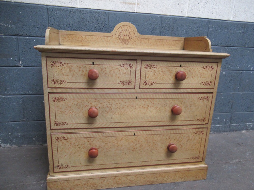 A Victorian painted pine chest of drawers with two short over two long drawers, decorated with scumbled graining, red stencilled borders, turned wooden knobs, and an upstand inscribed New Year Day 1894. View II