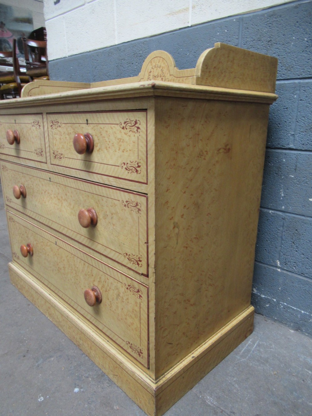 A Victorian painted pine chest of drawers with two short over two long drawers, decorated with scumbled graining, red stencilled borders, turned wooden knobs, and an upstand inscribed New Year Day 1894. View VI
