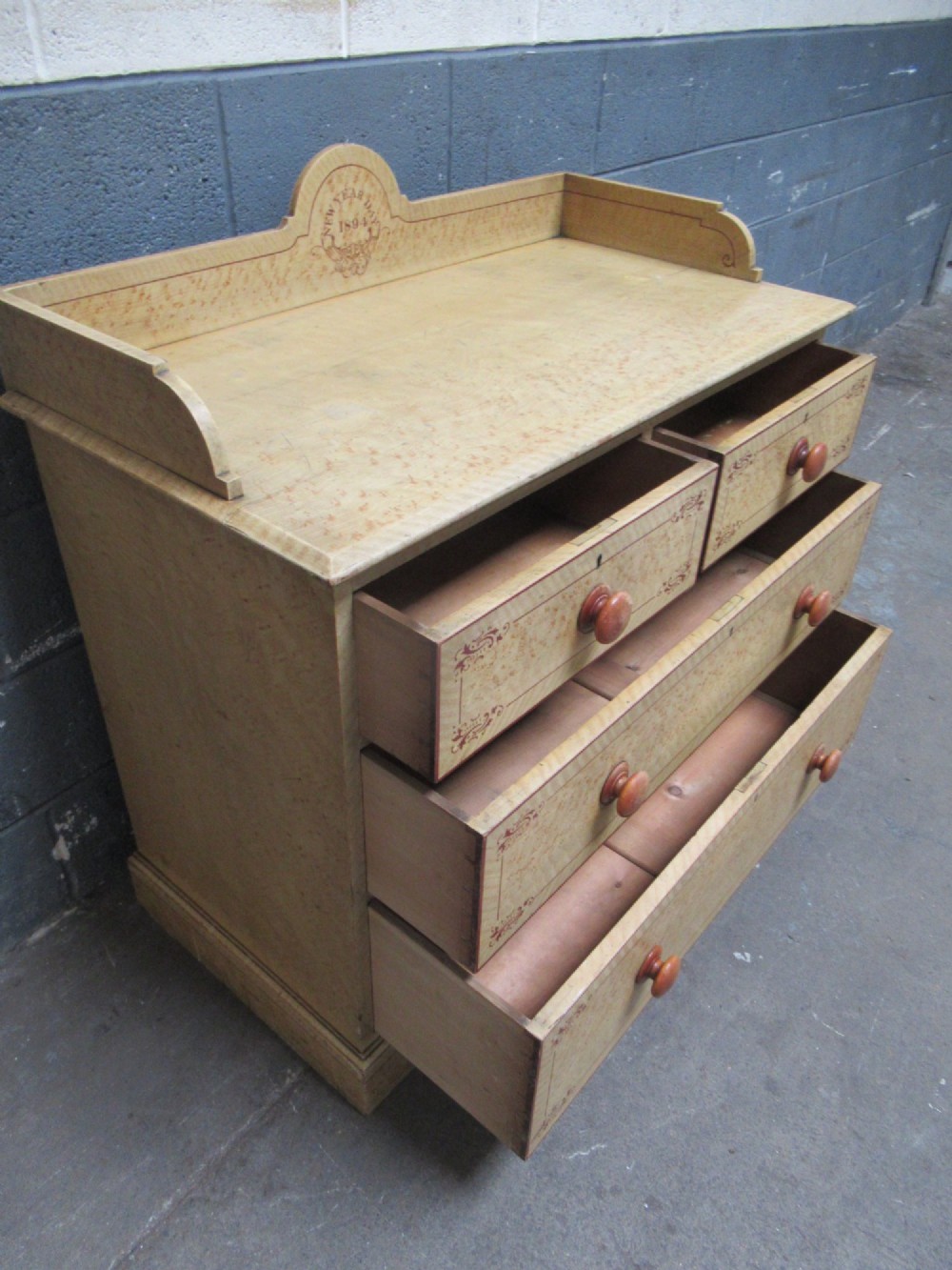A Victorian painted pine chest of drawers with two short over two long drawers, decorated with scumbled graining, red stencilled borders, turned wooden knobs, and an upstand inscribed New Year Day 1894. View X