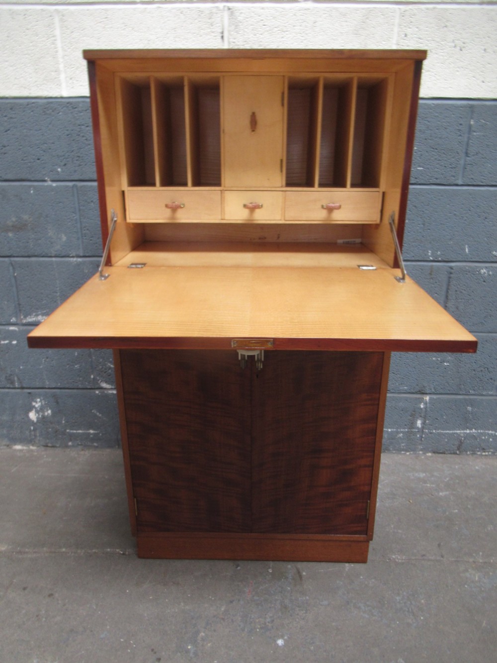 An Art Deco writing bureau in dark brown veneered wood featuring an open fall-front flap that reveals a light-coloured fitted interior with drawers and pigeonholes.